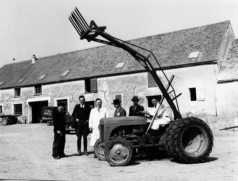 1953 - Mr JCB (third from left) with employee Doug Hollingworth (seted) and customers in France (1920).jpg